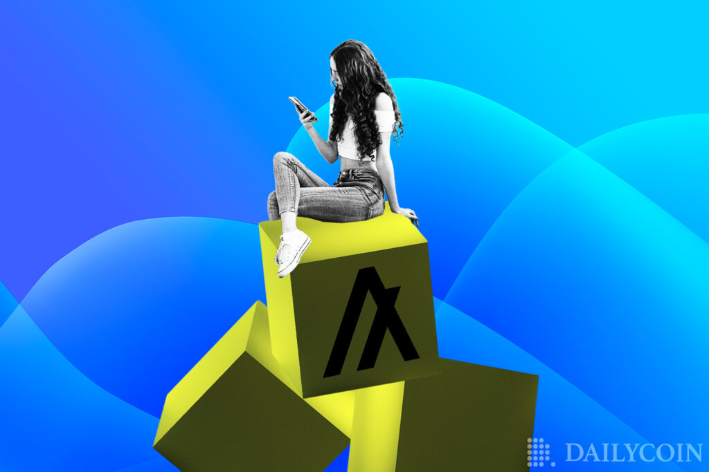A woman sitting on a bunch of yellow Algorand blocks while scrolling on her phone.