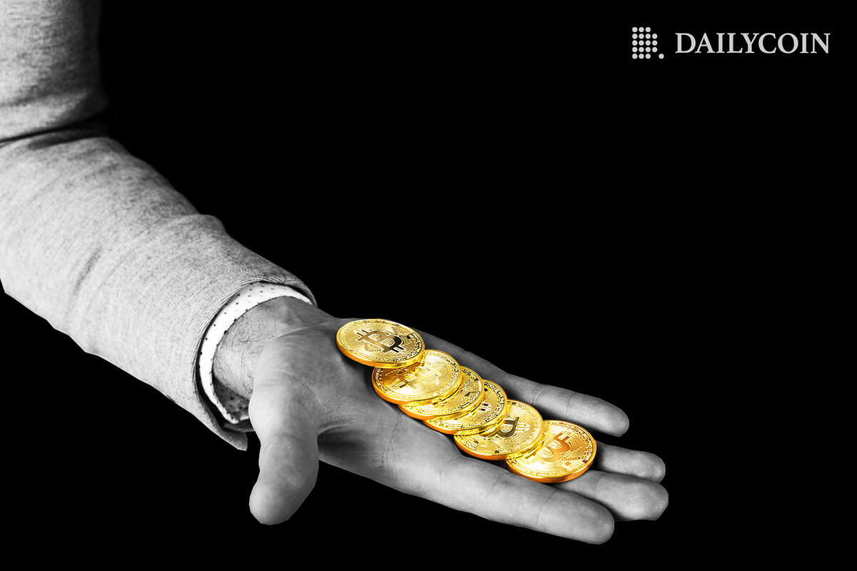 A human hand holding bitcoins.