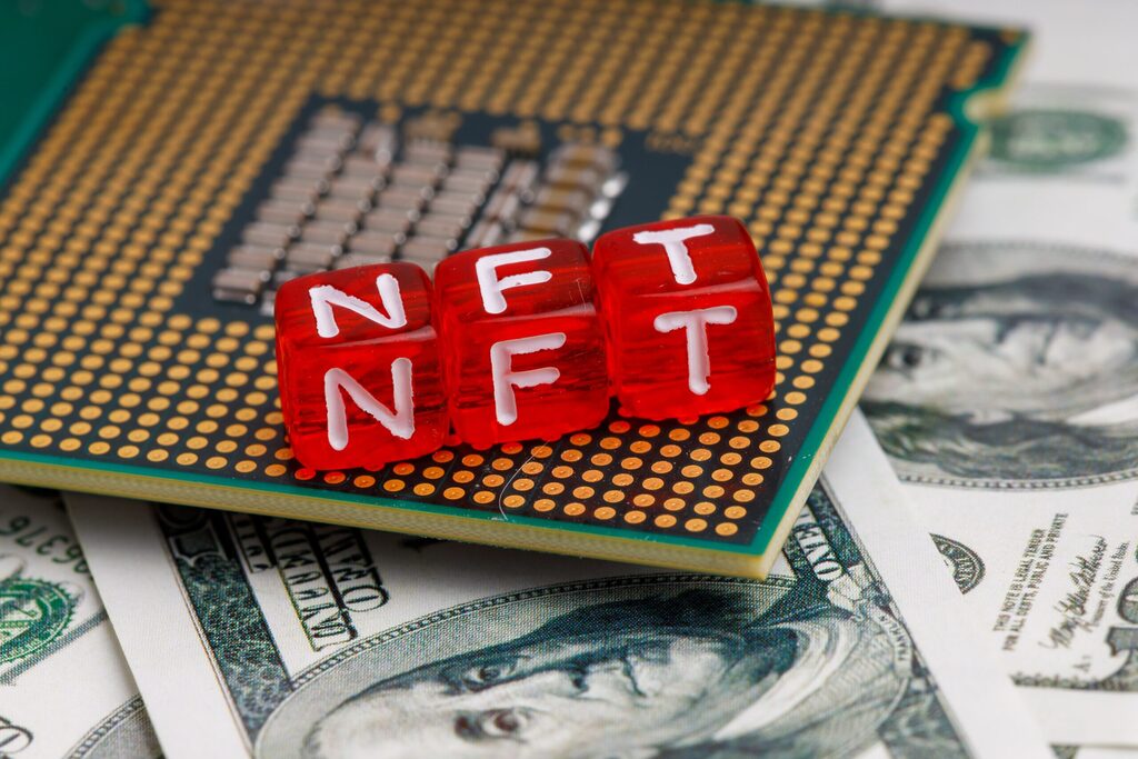 Three red dices spelling "NFT" are put together on a computer part on a pile of cash. 