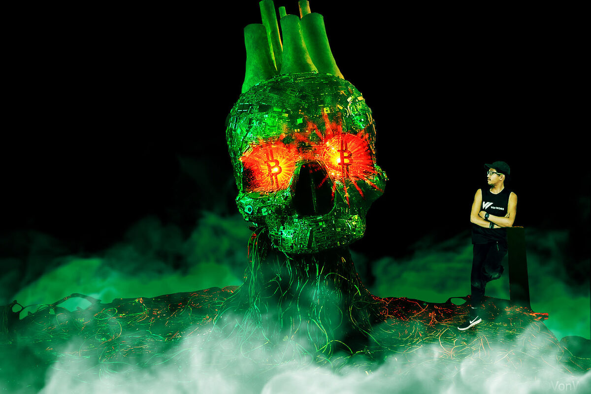 Artist standing next to a giant green skull with red Bitcoin eyes.