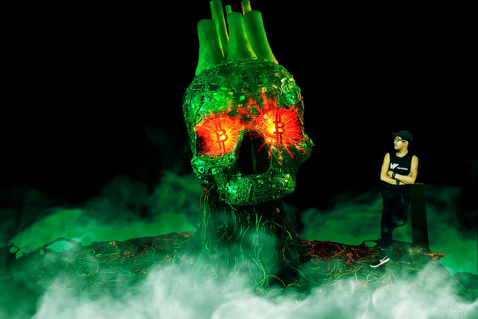 Artist standing next to a giant green skull with red Bitcoin eyes.