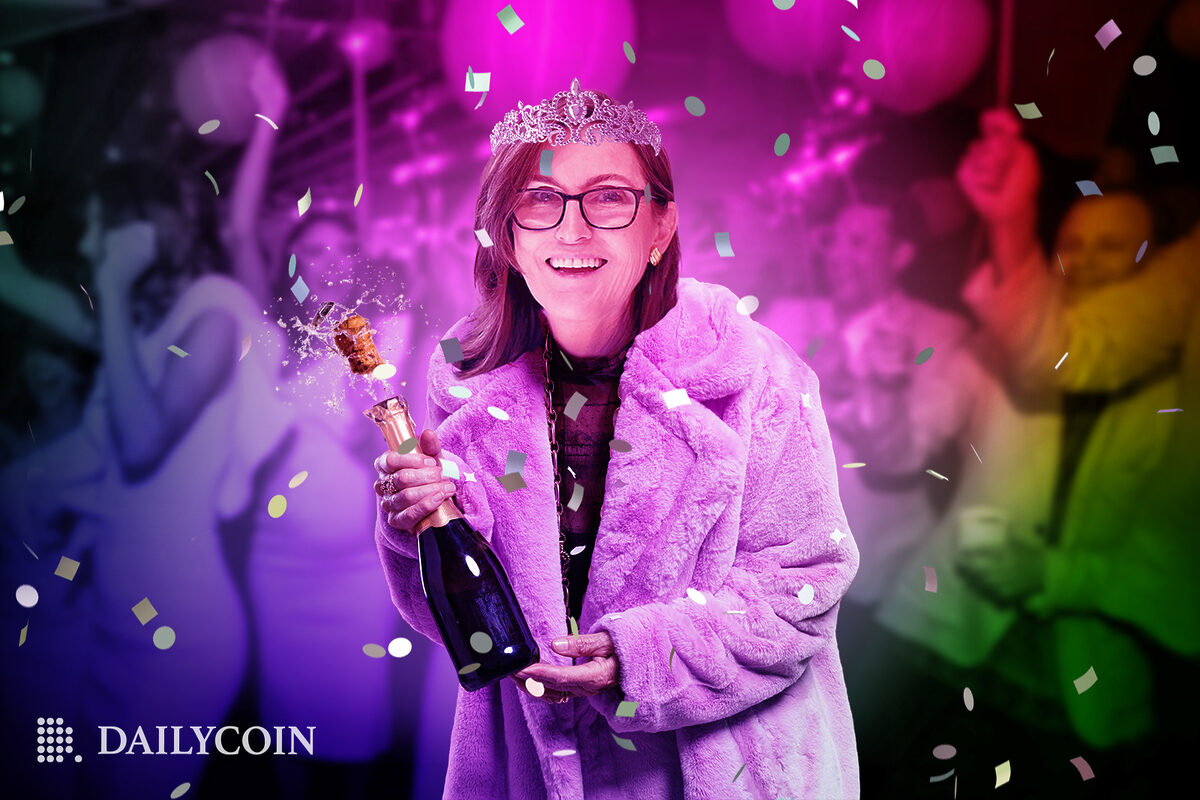 Cathie Wood in a pink coat holding a bottle of champagne