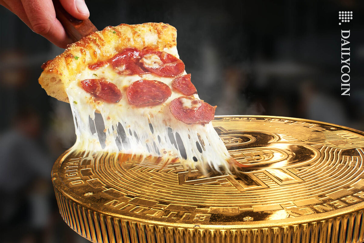A freshly baked slice of pizza being lifted out of a huge bitcoin.
