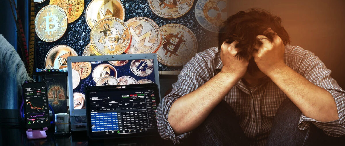 Distressed man with head in his hands sits in front of background of crypto coins.