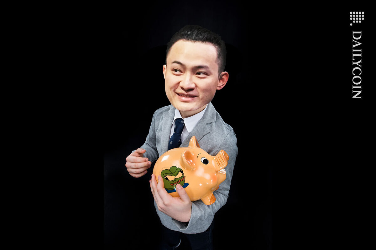 Justin Sun holding a piggy bank with a picture of angry Pepe the Frog on it.