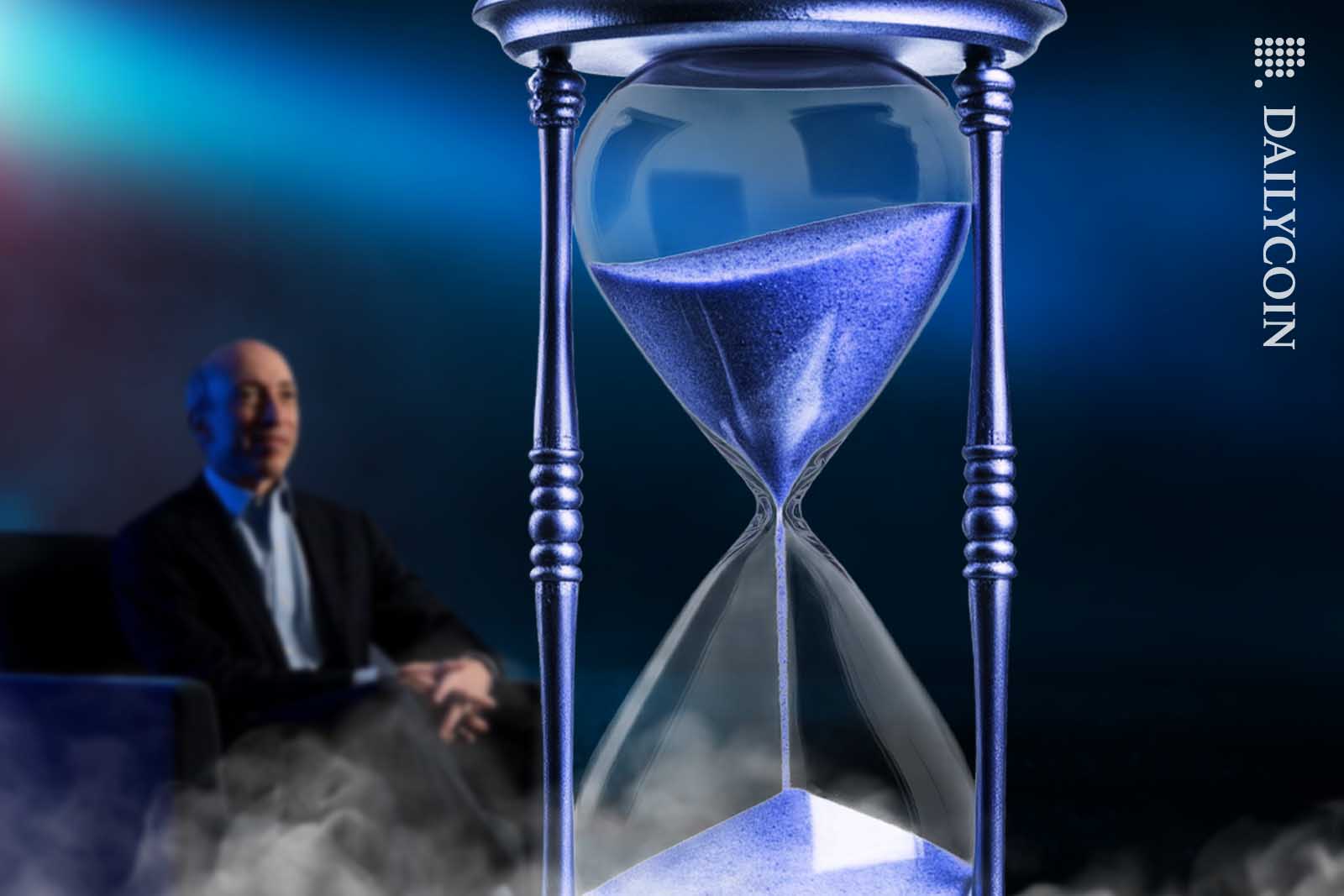 Gary Gensler sitting in the dark looking at a sand clock as time passing by.