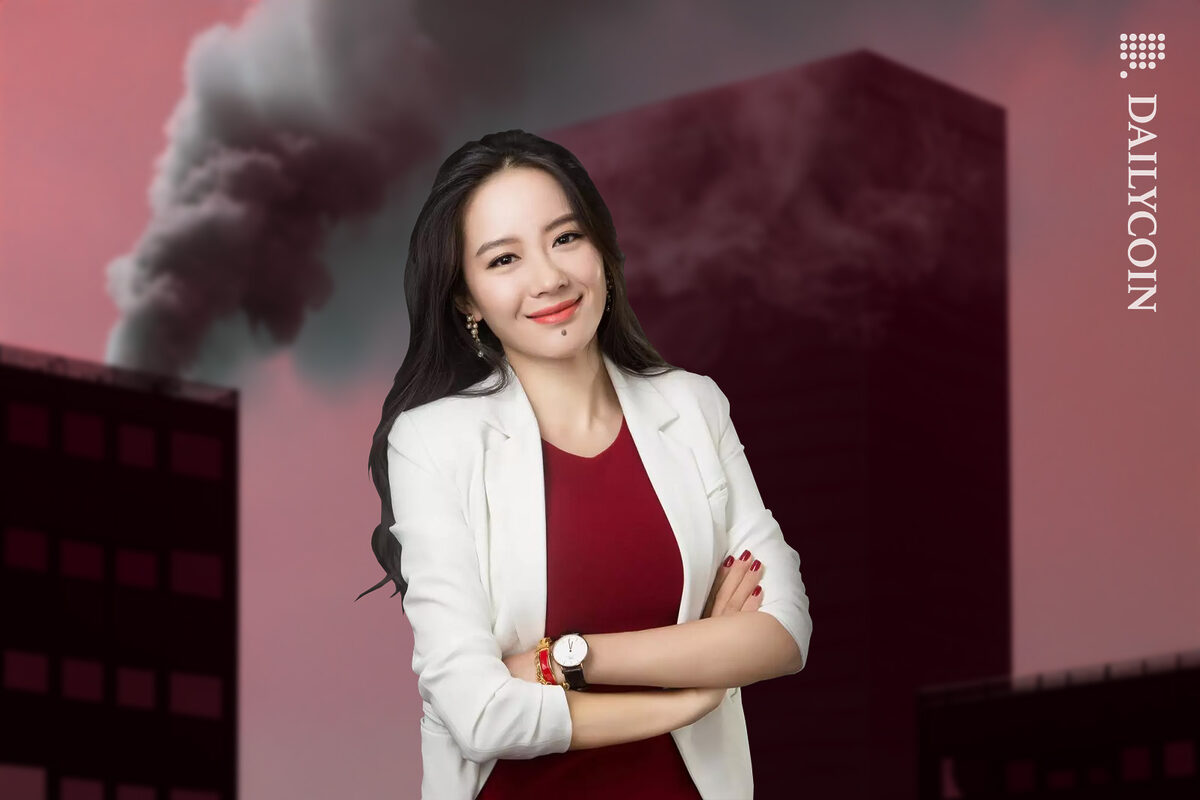Yi He of Binance standing in front of an office building with some smoke coming out of it.