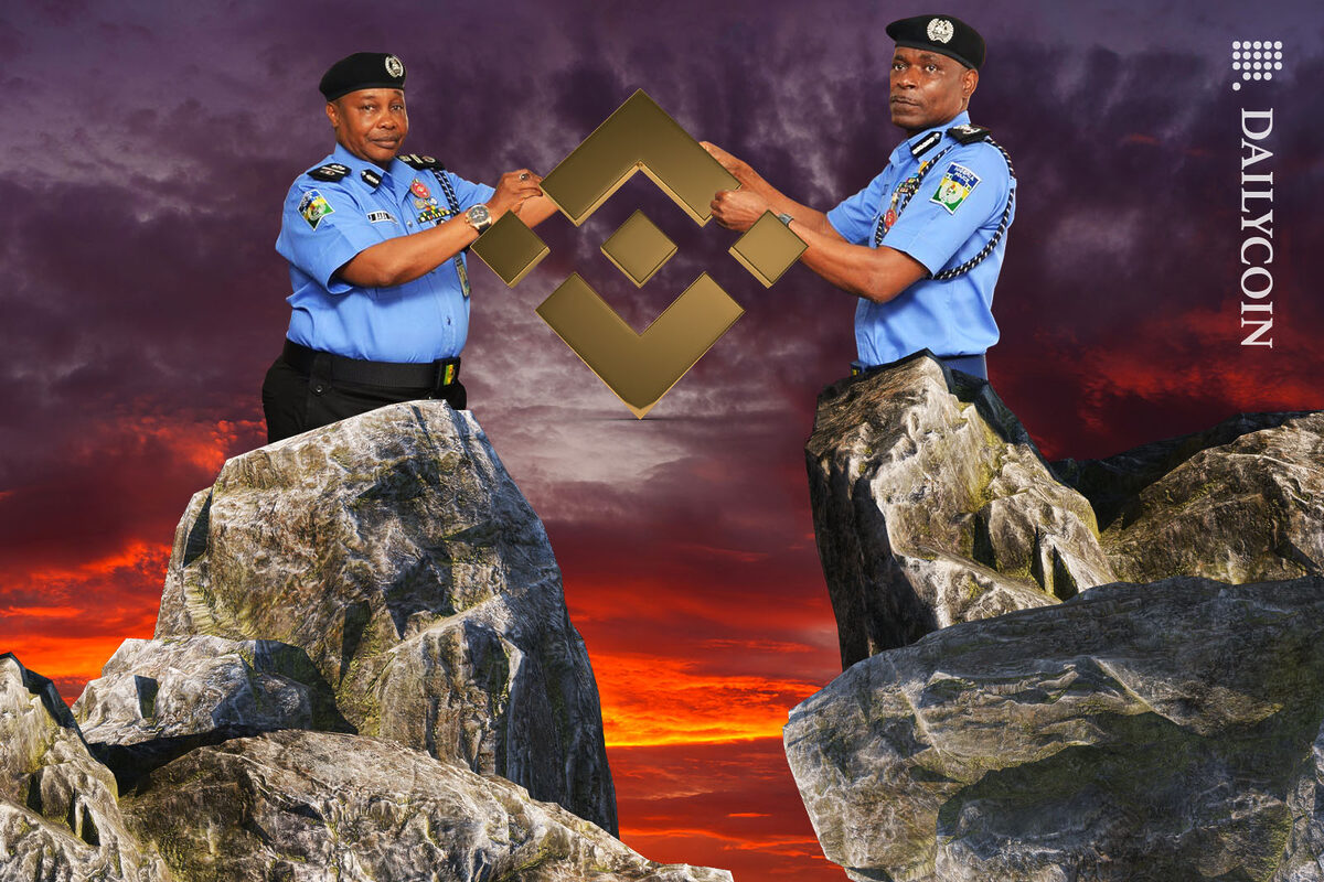 Two Nigerian police officers holding a Binance logo over a cliff.