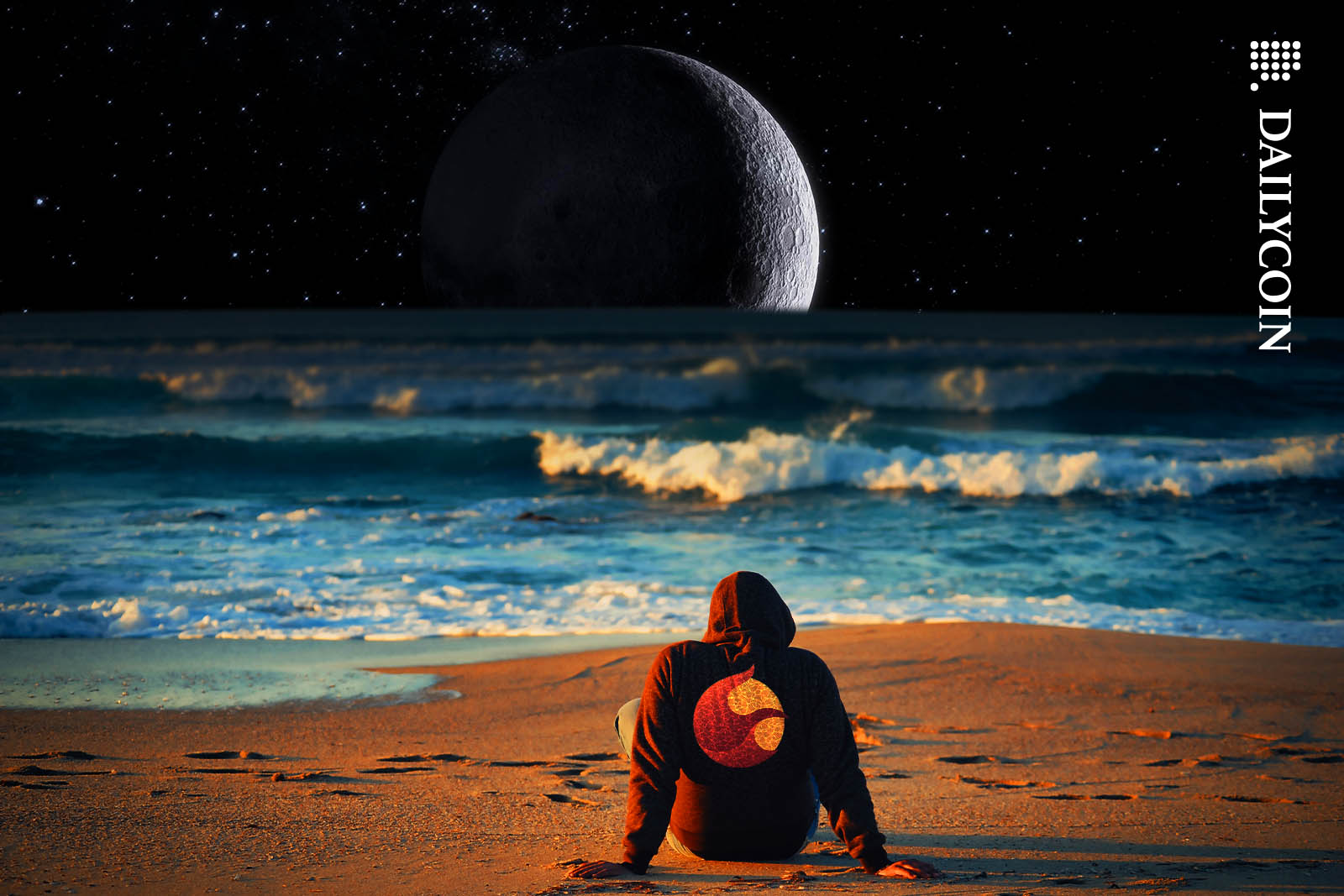 Man in a Tera Luna hoodie staring at the moon on a beach.