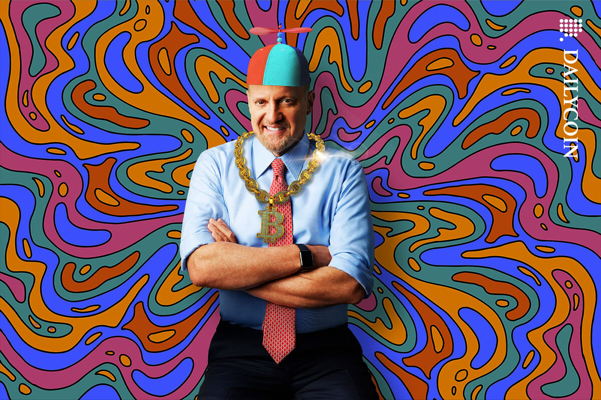 Jim Cramer posing in a clown's hat and a super blingy Bitcoin chain, smiling confidently.