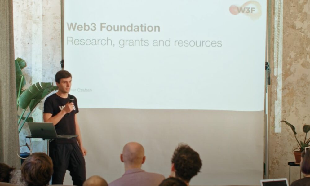 Peter Czaban speaking to an audience with a board behind him saying "Web3 Foundation: research, Grants and Resources."