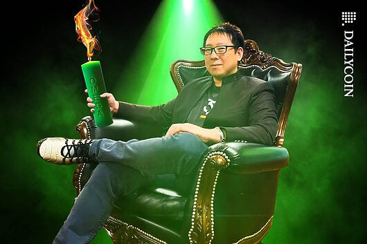 Samson Mow sitting in an armchair holding a green Omega candle.